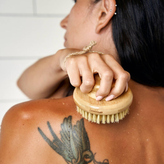 Person using a wooden brush on their back with a white tiled wall in the background