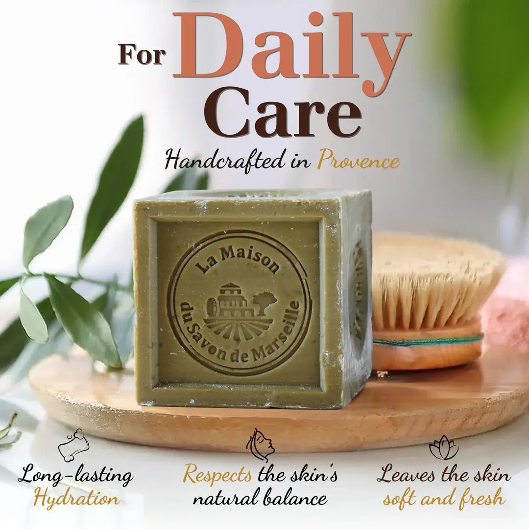 Green bar of soap with branding on a wooden tray with a brush and leaves in the background, labeled 'For Daily Care Handcrafted in Provence'.