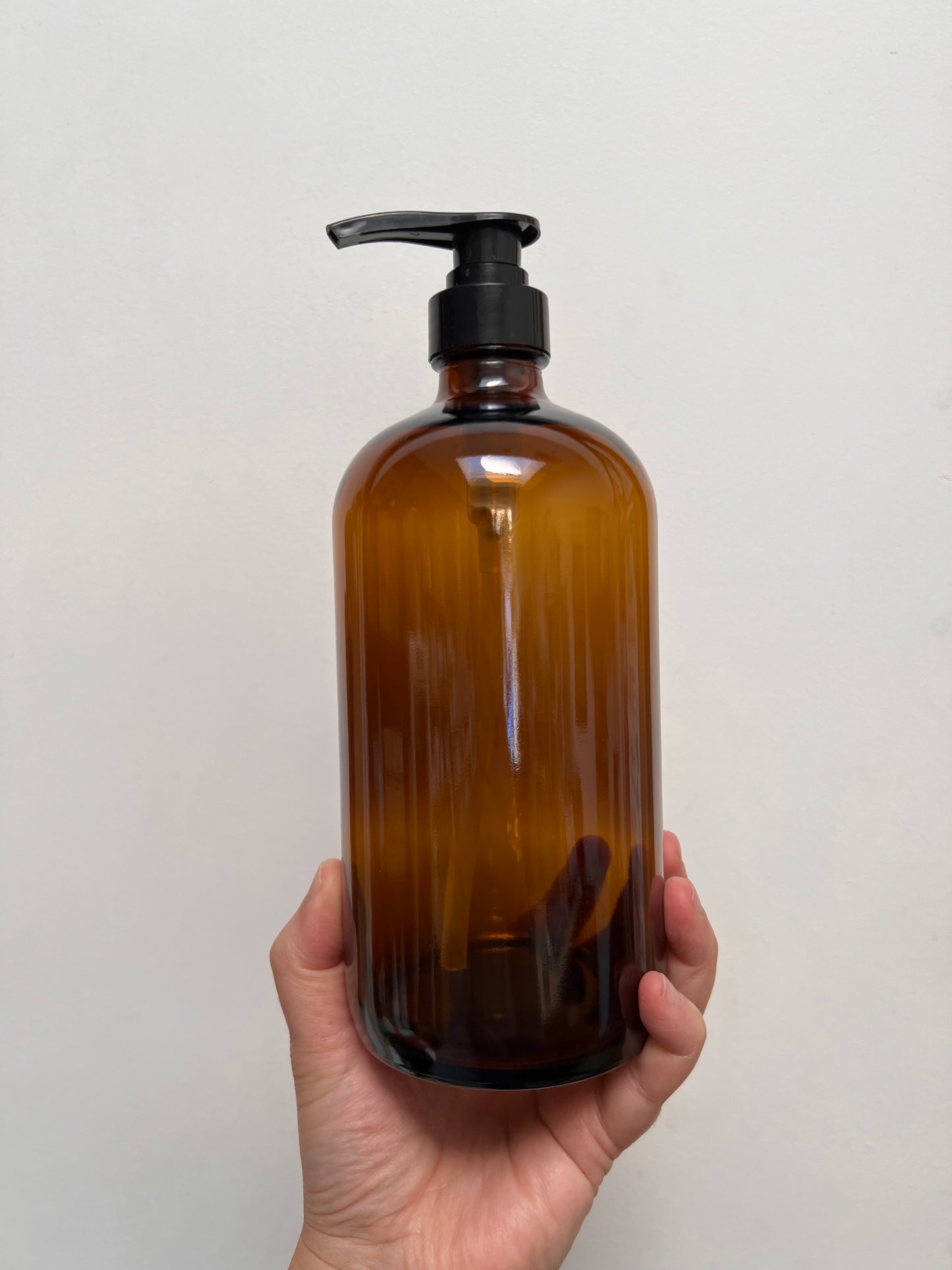 Hand holding a brown glass bottle with a black pump against a light gray background