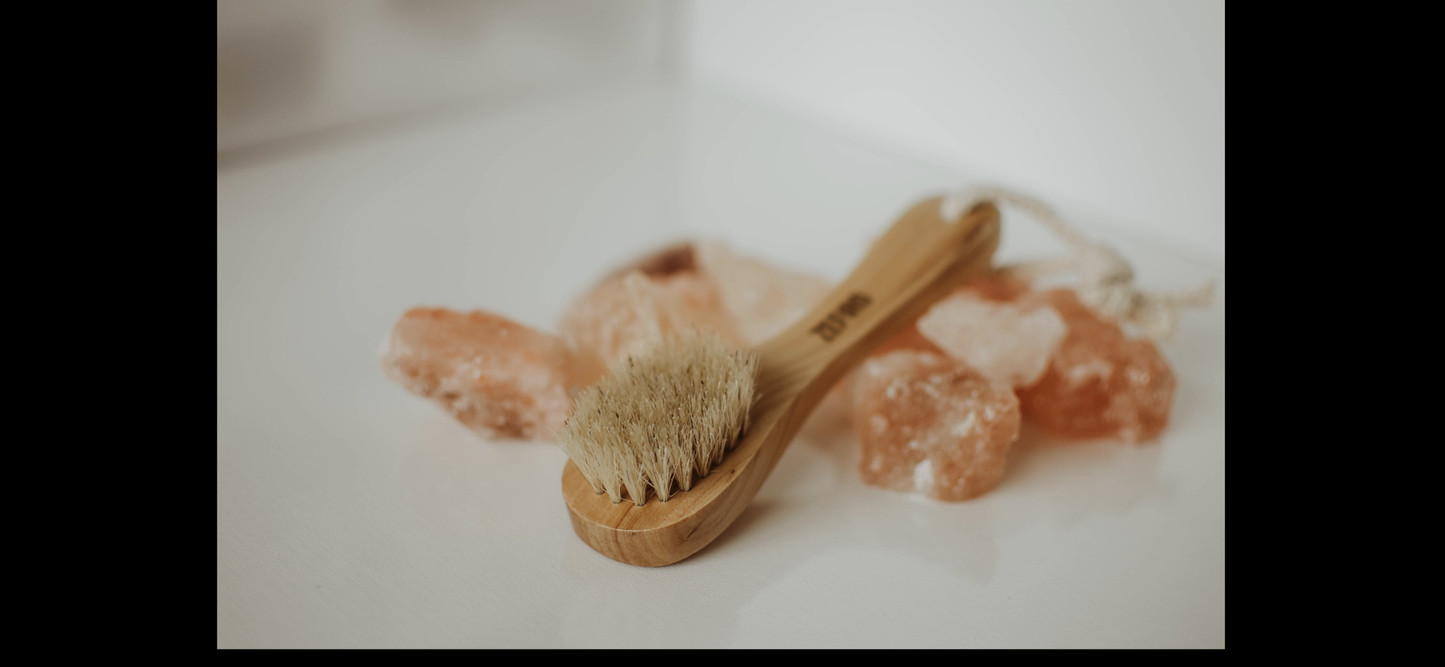Wooden brush with bristles on a white surface with pink sea salt crystals.