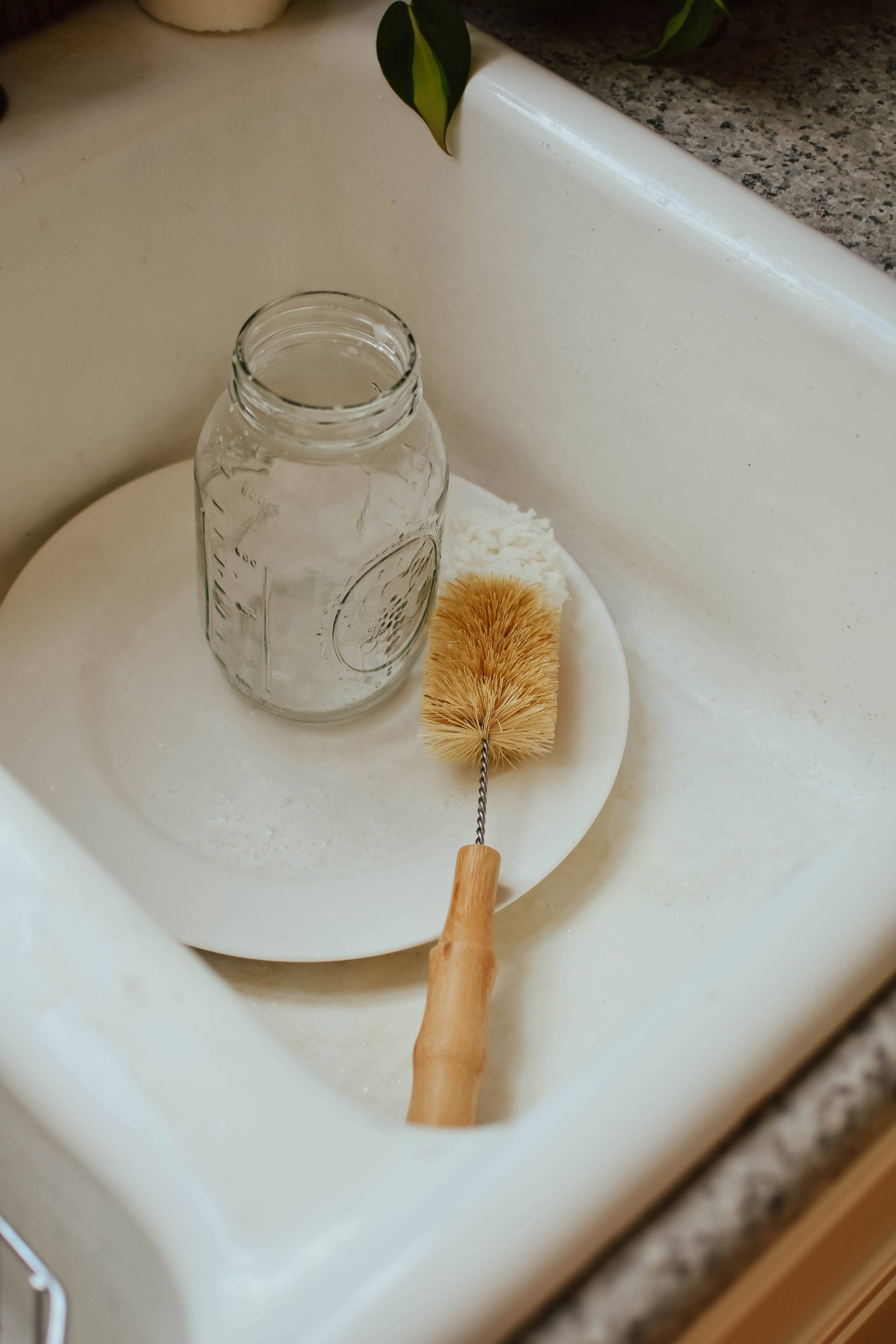 Mason jar with a cleaning brush on a white plate in a sink