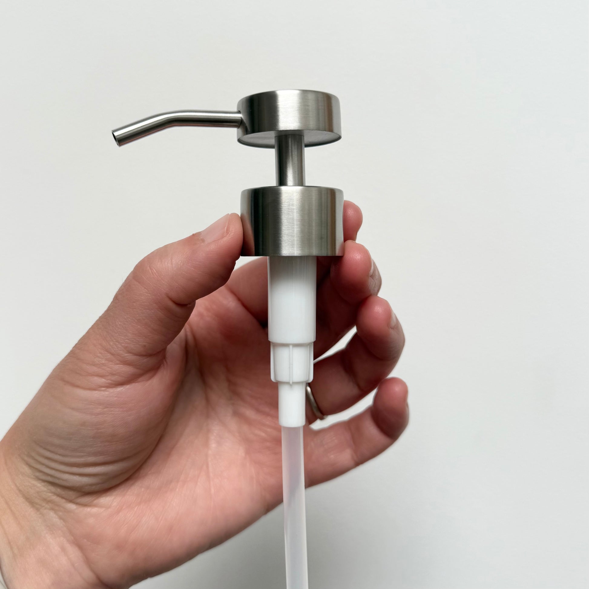 Hand holding a stainless steel pump top that fits on 16 ounce glass bottle.