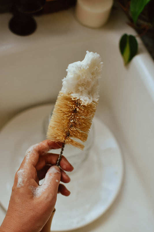 Hand holding a scrubbing brush with soap suds over a sink