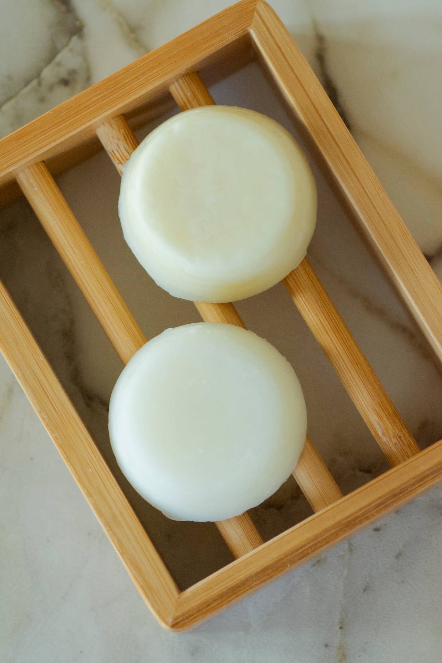 Two round white soaps on a wooden rack with a marble background