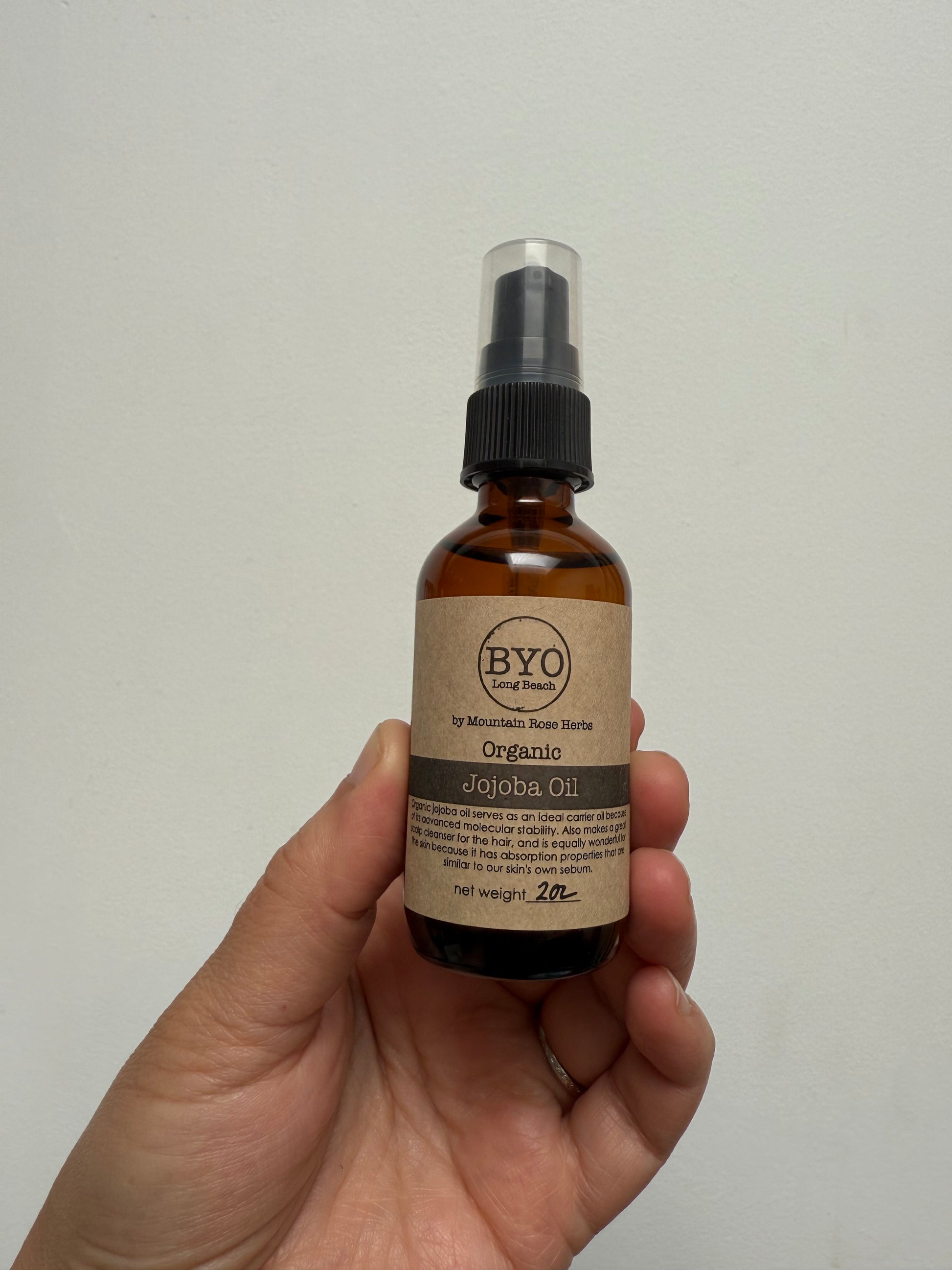 Hand holding an amber glass bottle labeled Jojoba Oil