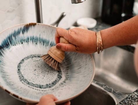 Person scrubbing a ceramic bowl with a brush in a kitchen setting