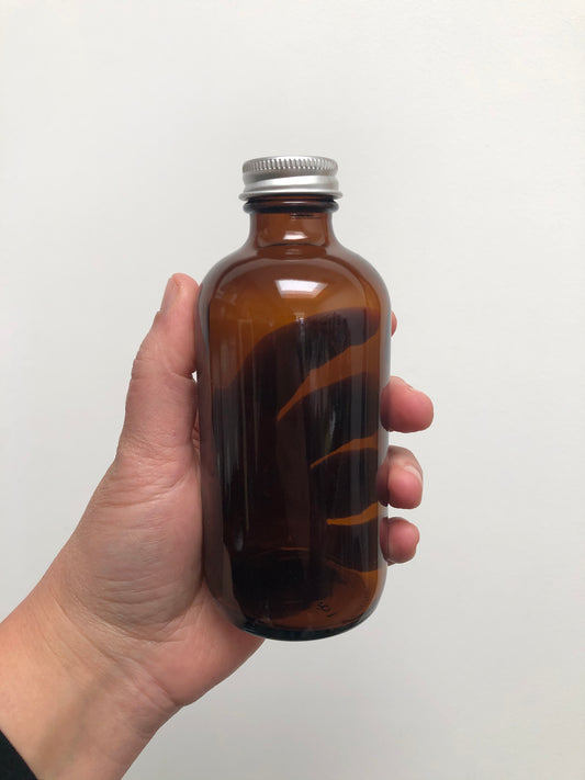 Hand holding a brown glass bottle with a silver cap against a white background