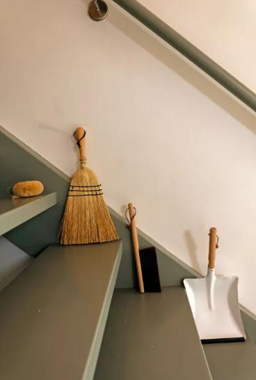 Series of brooms and cleaning brushes leaning against a white wall on grey stairs.