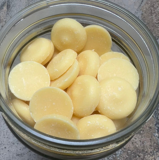 Jar filled with light yellow cocoa butter coins. Each coin is approximately the diameter of a quarter and about 1/8” thick.