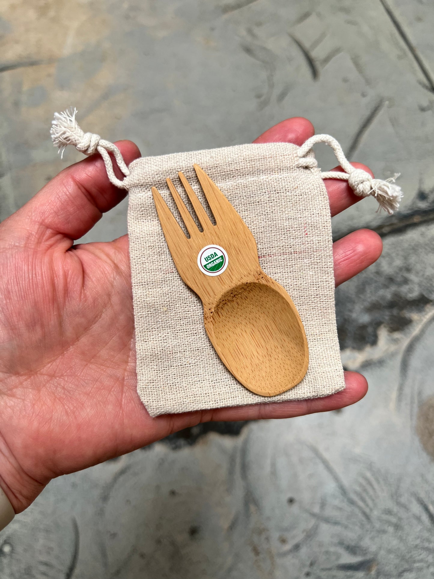 Hand holding a cotton drawstring pouch with a bamboo spork on top to show the fit.