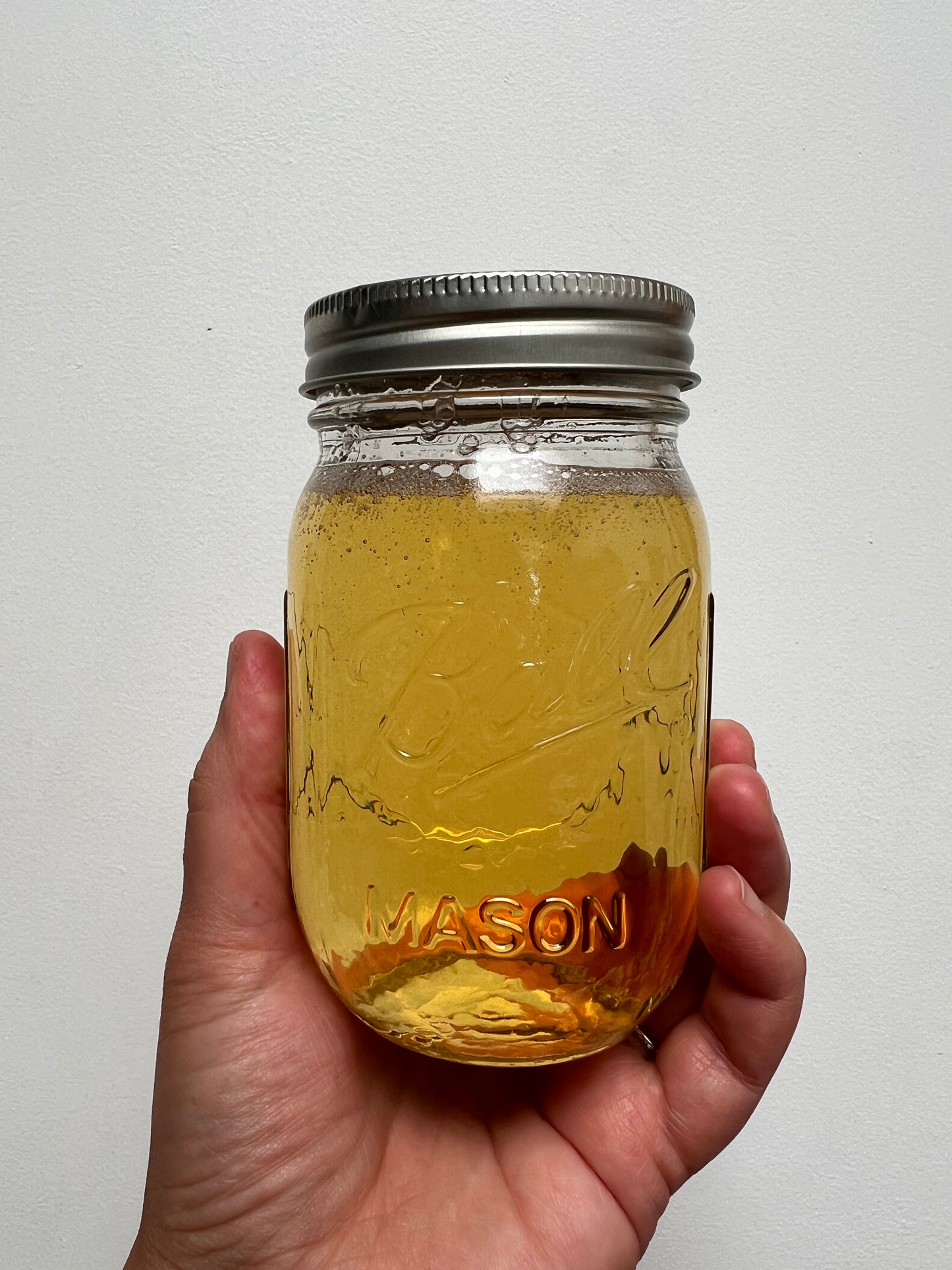 Hand holding a pint size regular mouth mason jar with golden color liquid soap.