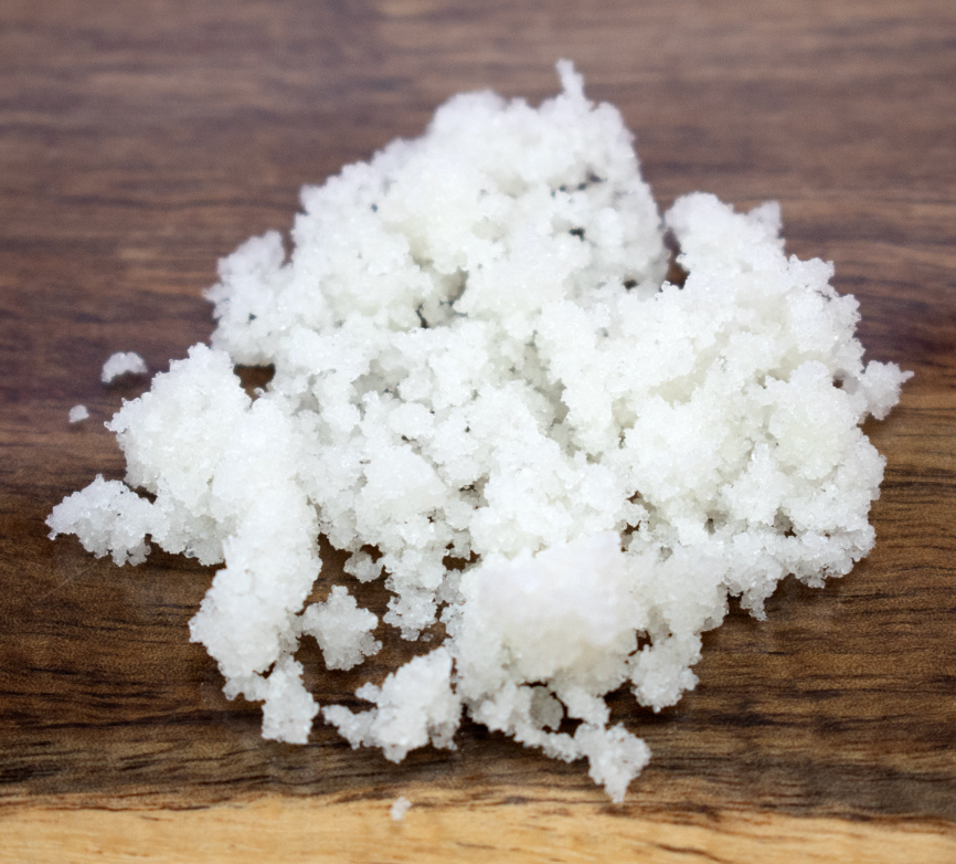A pile of coarse white salt crystals resting on a dark brown wooden surface.