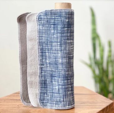 Roll of blue and gray checkered fabric on a wooden stand with a blurred plant in the background