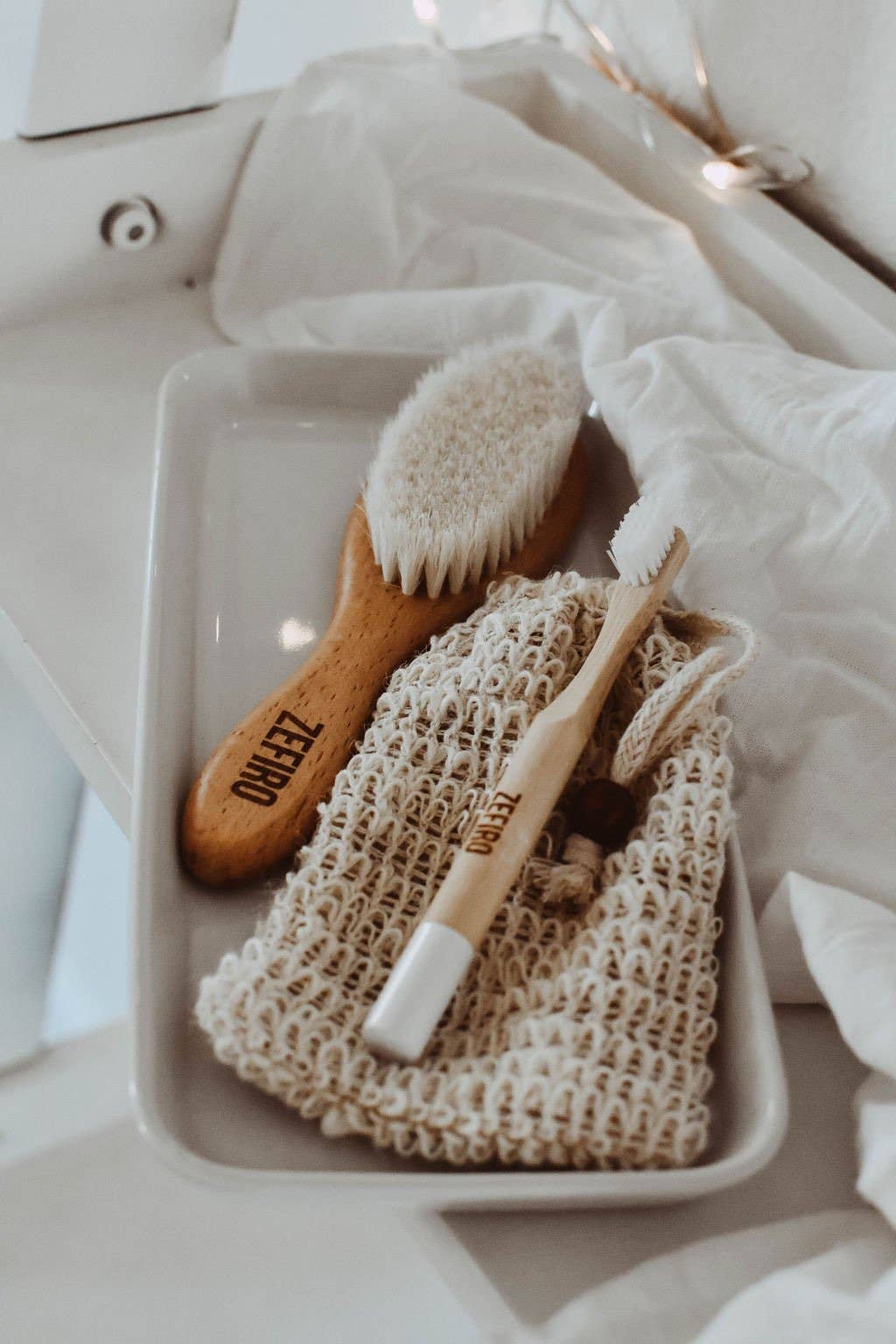 Wooden brush, white toothbrush, and mesh bag on a white plate with a soft focus background.