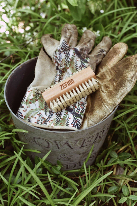 Gardening tools including gloves and a brush in a metal container on grass