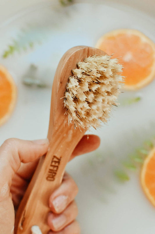 Hand holding a wooden brush with bristles over a background of oranges and water.
