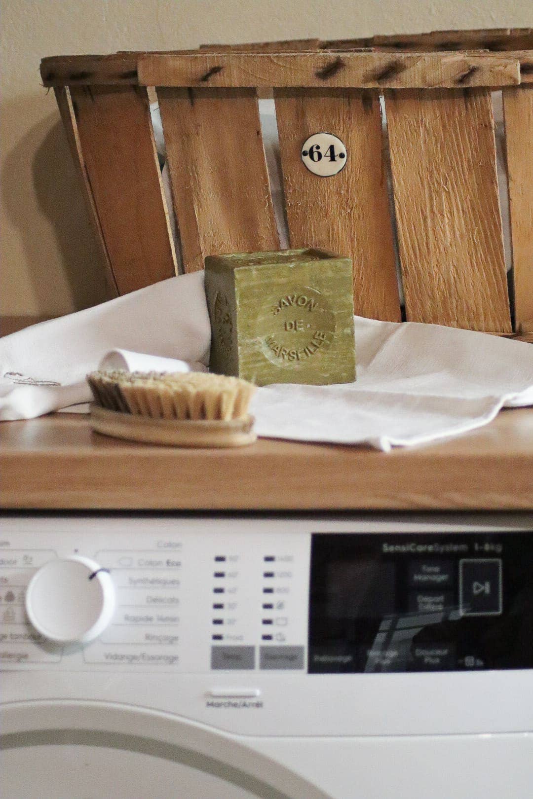 Wooden surface with a bar of soap, brush, and towel in front of a washing machine.