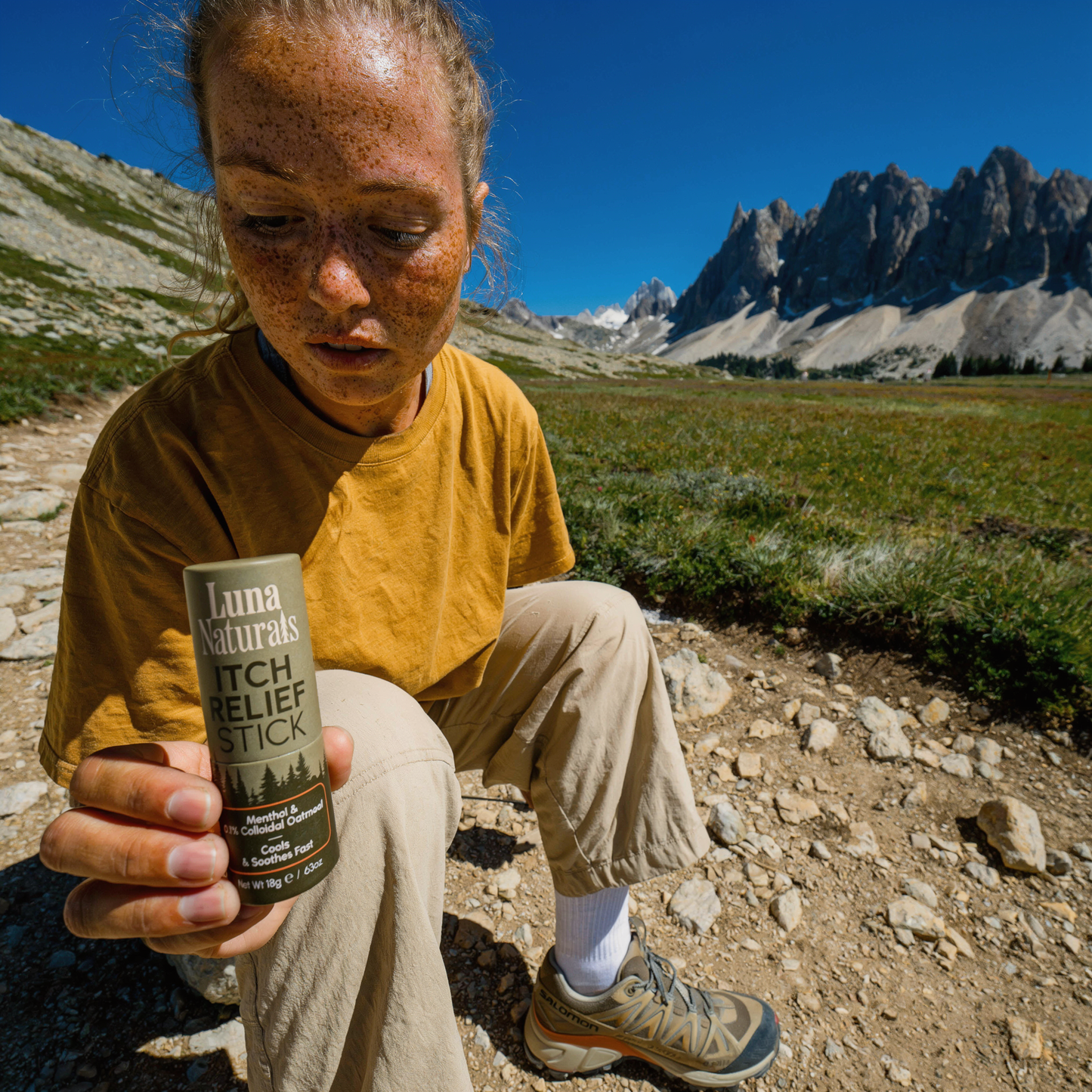 Person holding a Luna Naturals itch relief stick in a mountainous landscape