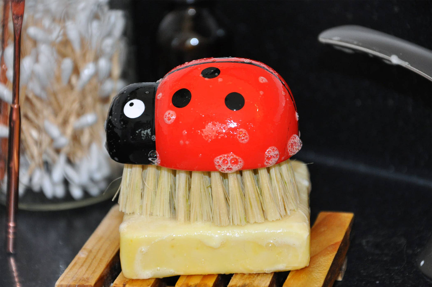 Soap shaped like a ladybug on a bar of soap with a brush on a wooden block.