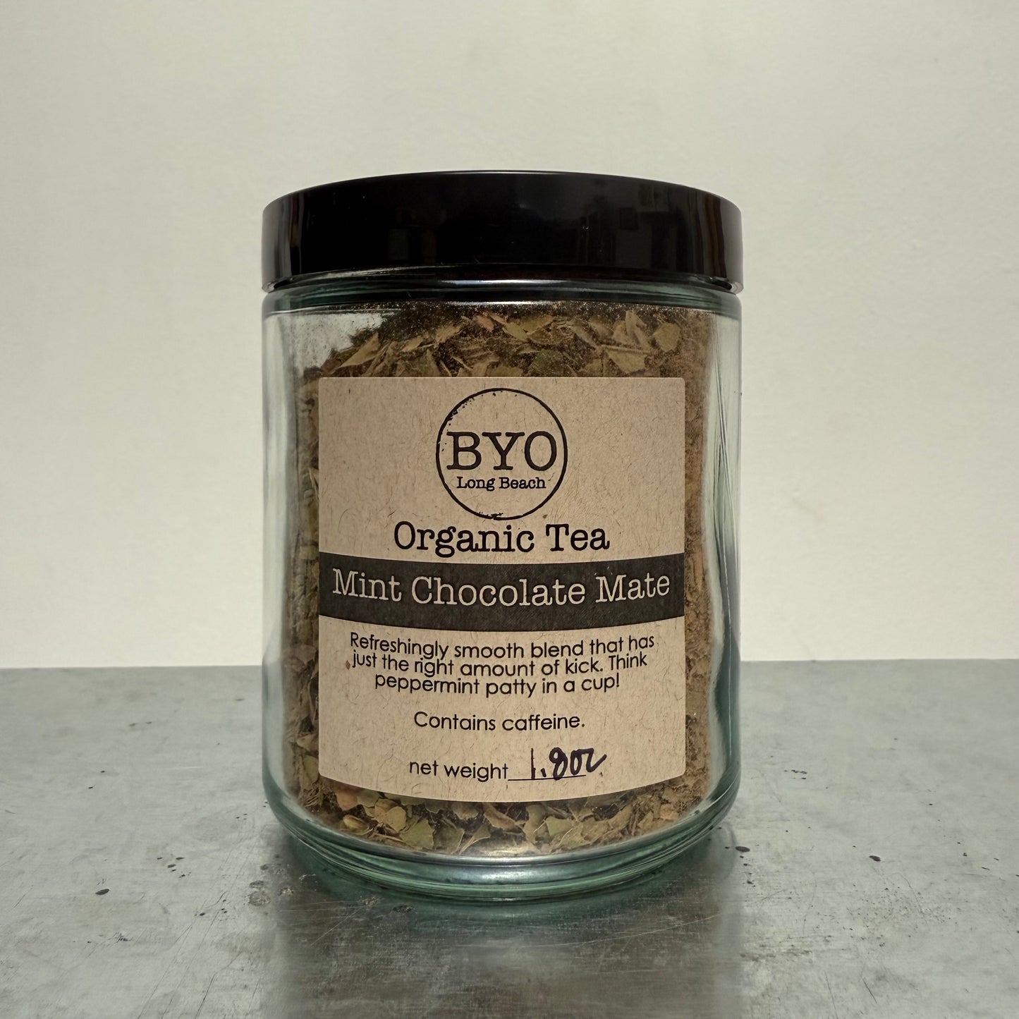 Jar of organic tea labeled 'Mint Chocolate Mate' by BYO on a gray surface.