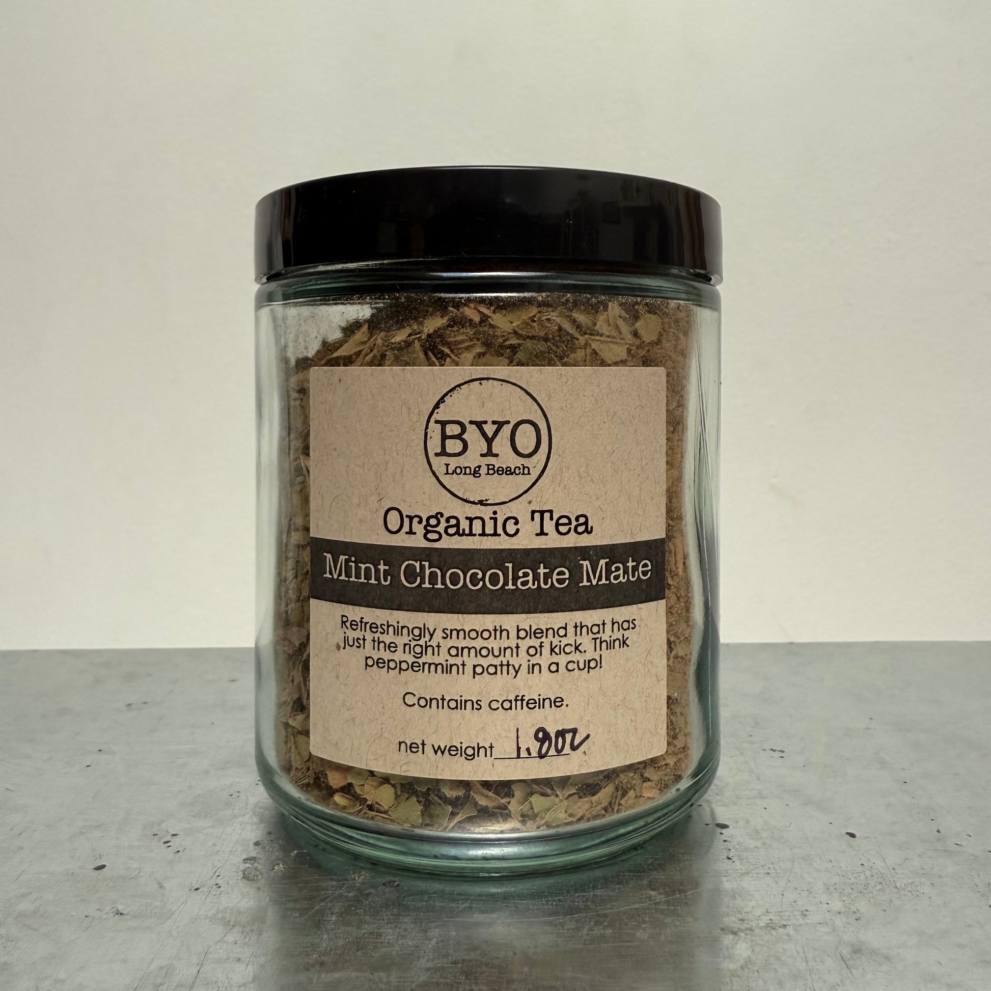 Jar of organic tea labeled 'Mint Chocolate Mate' by BYO on a gray surface.