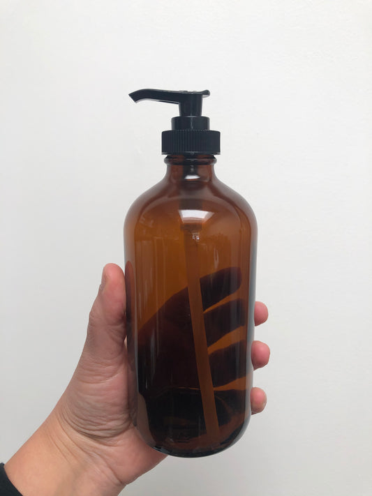 A hand holding a brown glass bottle with black plastic pump top.