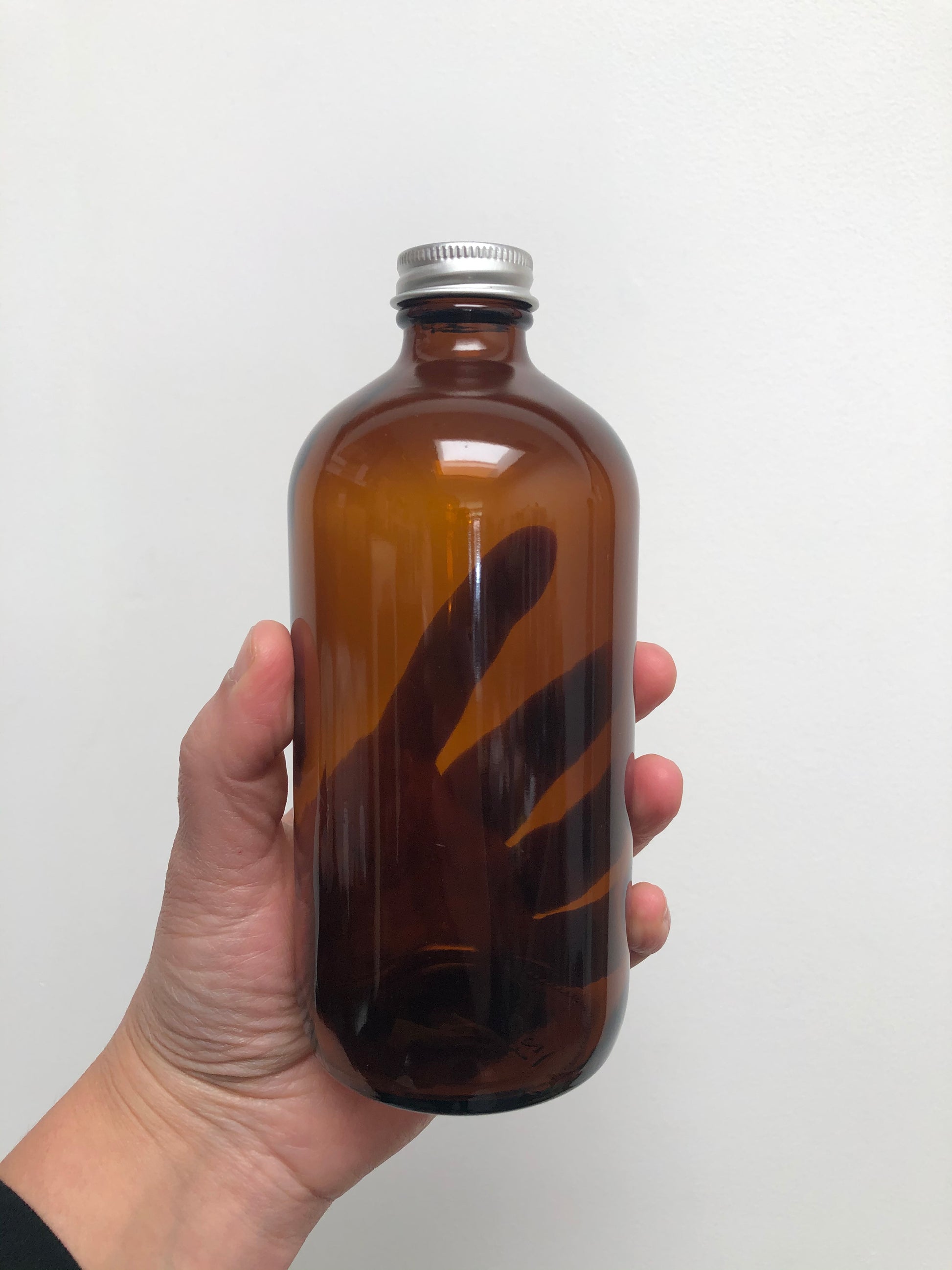 Hand holding a brown glass bottle with a silver cap on a white background