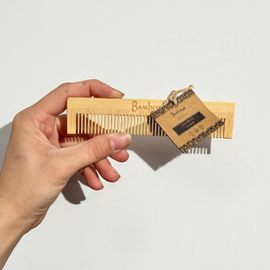 Hand holding a wooden comb with a matching packaging label on a light background