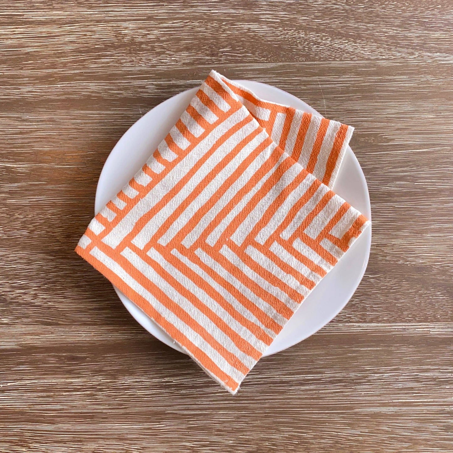 Orange and white striped napkin on a white plate with a wooden background