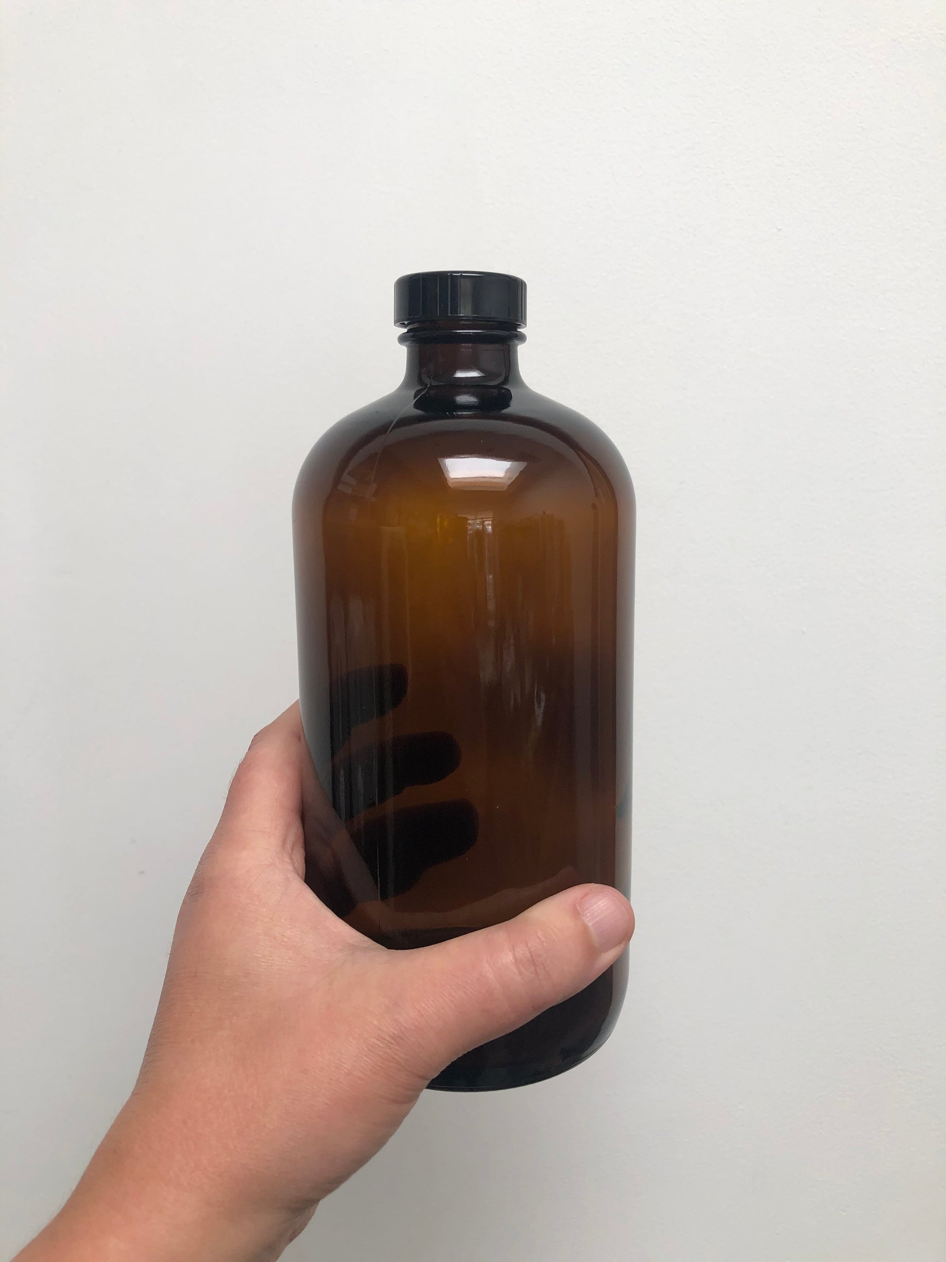 Hand holding a brown bottle with a black cap on a white background