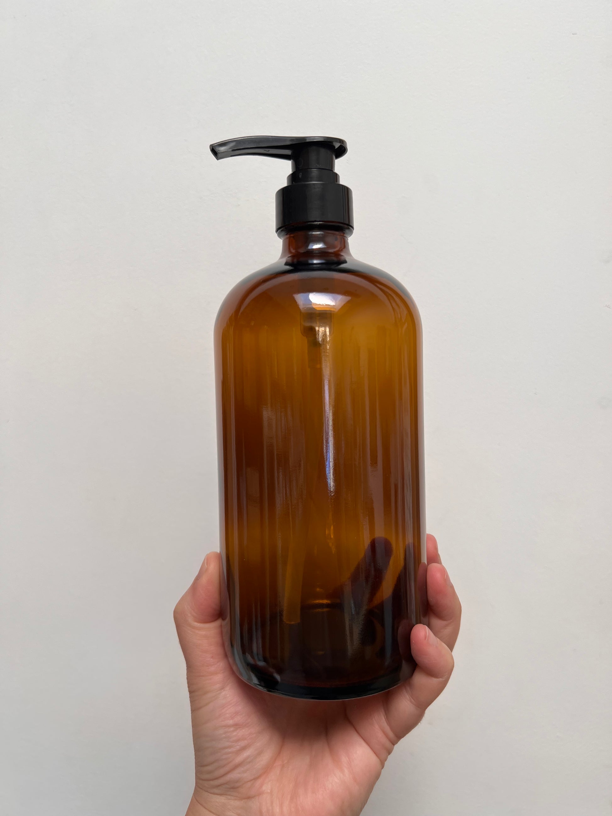 Hand holding a brown glass bottle with a black pump against a light gray background