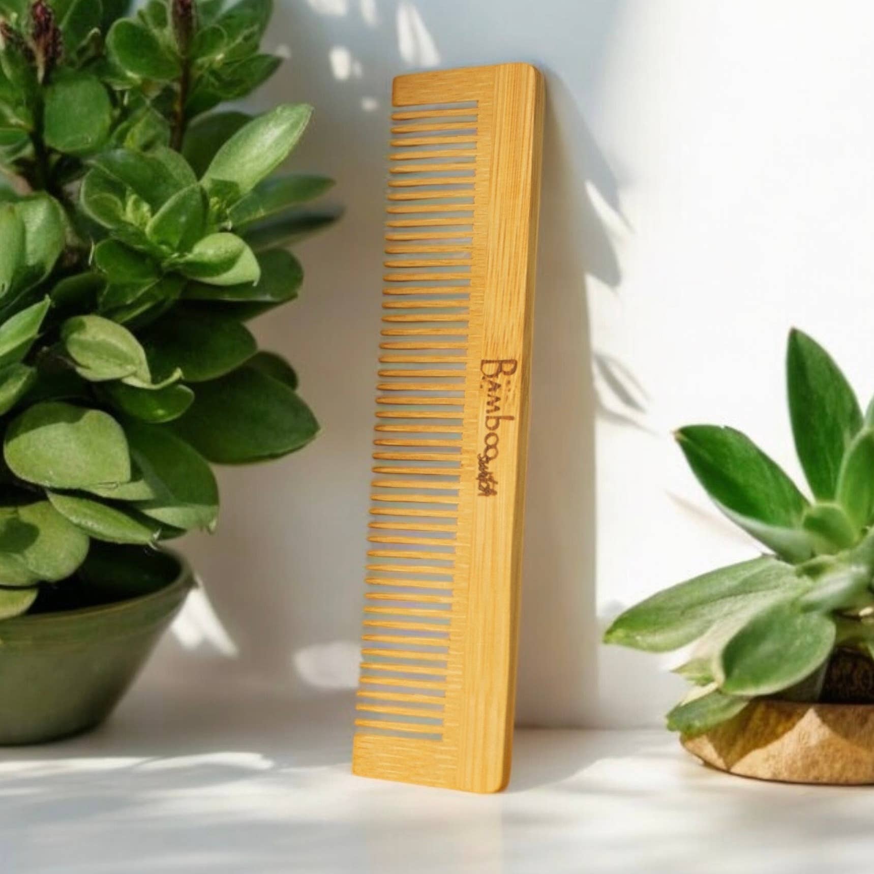Wooden comb with 'Bamboo' engraving on a white surface with plants in the background
