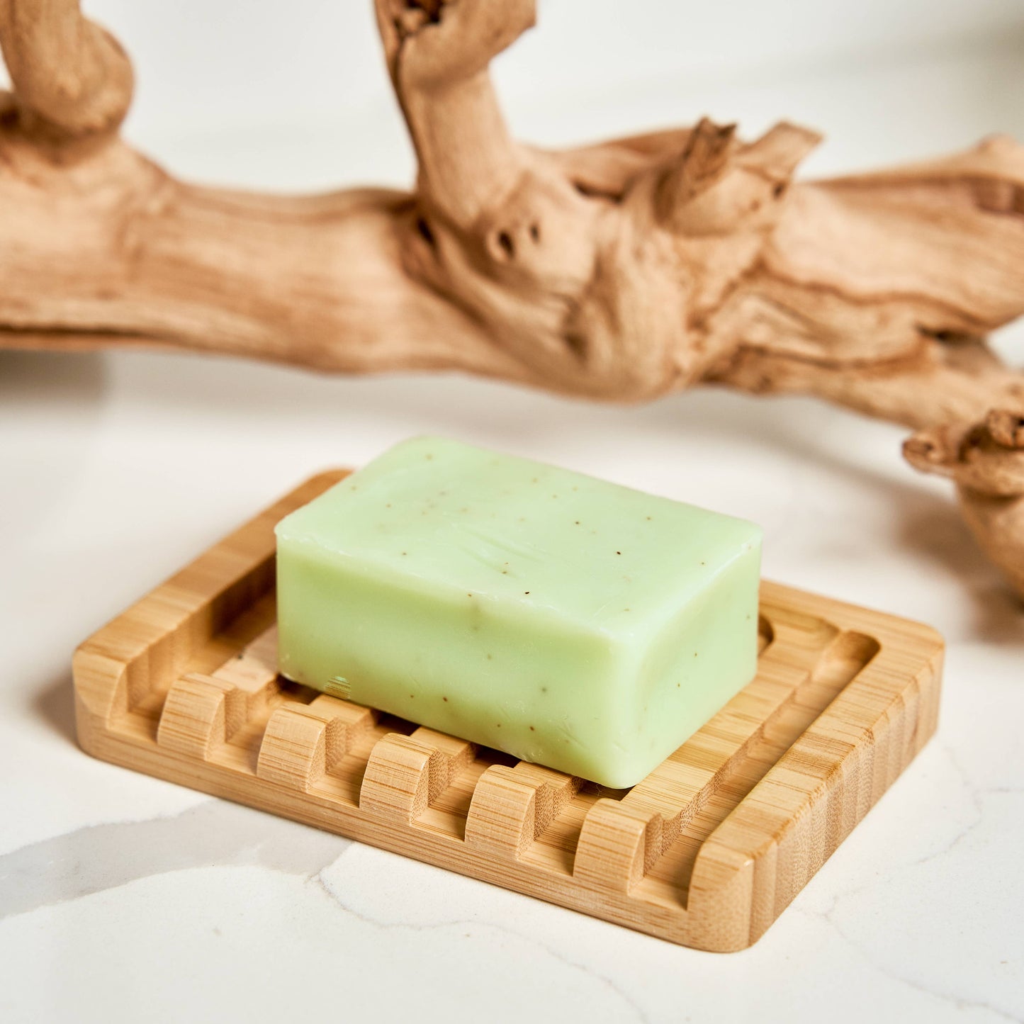 Green bar of soap on a wooden soap dish with a natural wood background
