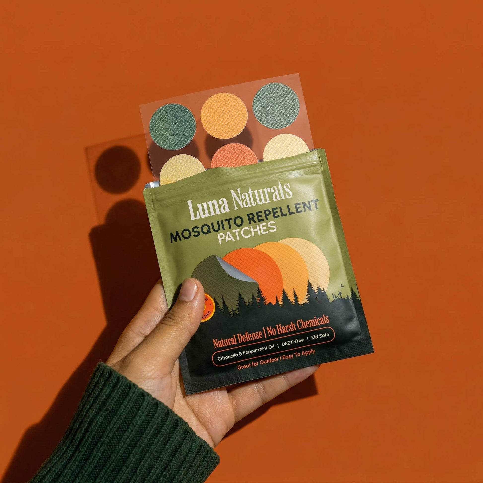 Hand holding a package of Luna Naturals mosquito repellent patches against an orange background