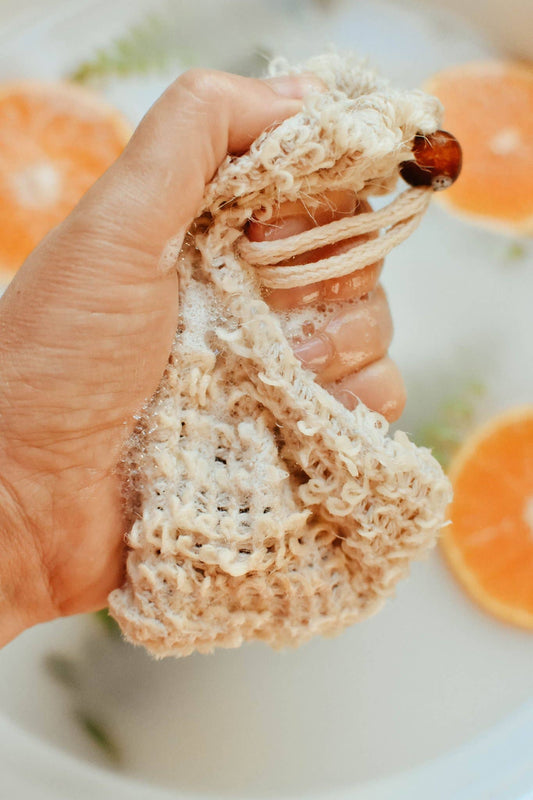 Hand holding a textured beige sponge with oranges in the background
