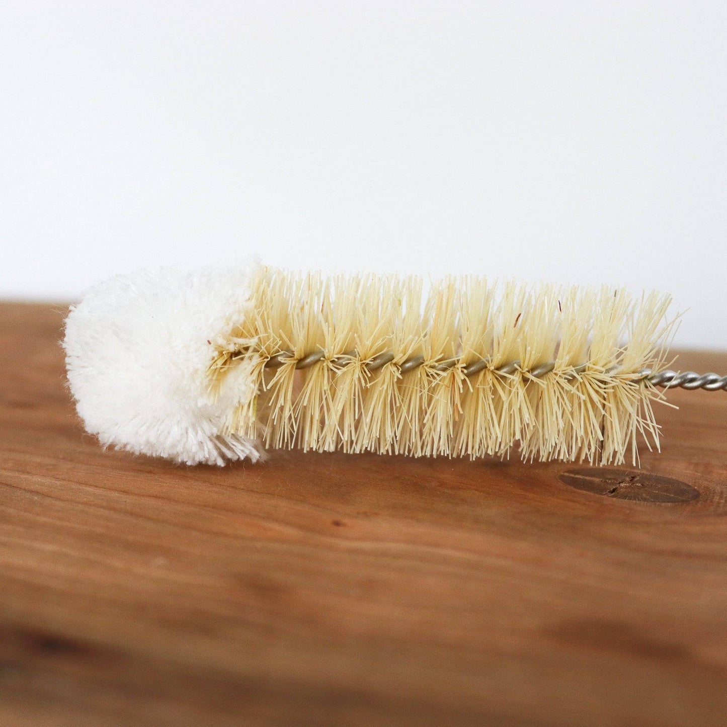 Cleaning brush with white bristle head and beige bristle head on a wooden surface