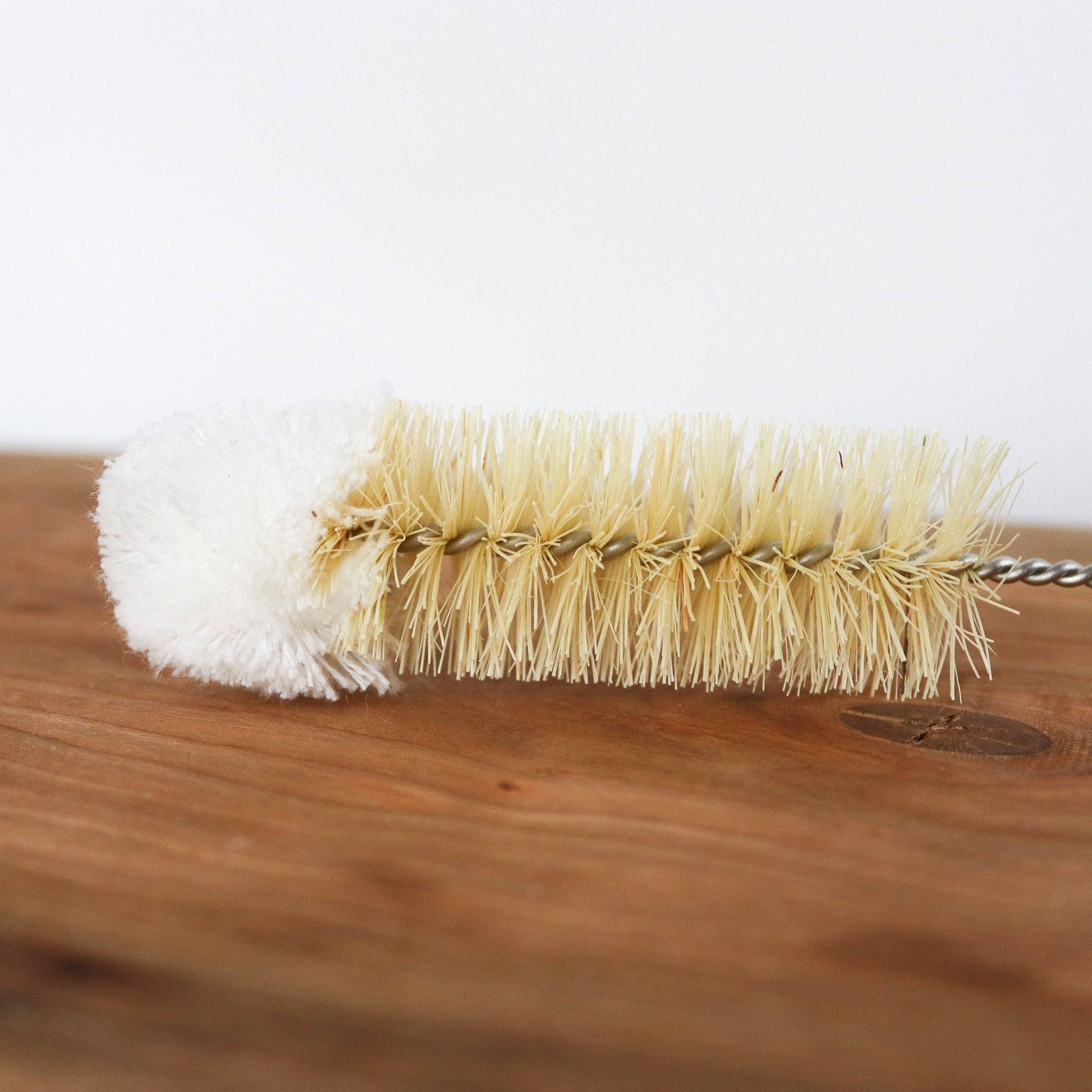 Cleaning brush with white bristle head and beige bristle head on a wooden surface