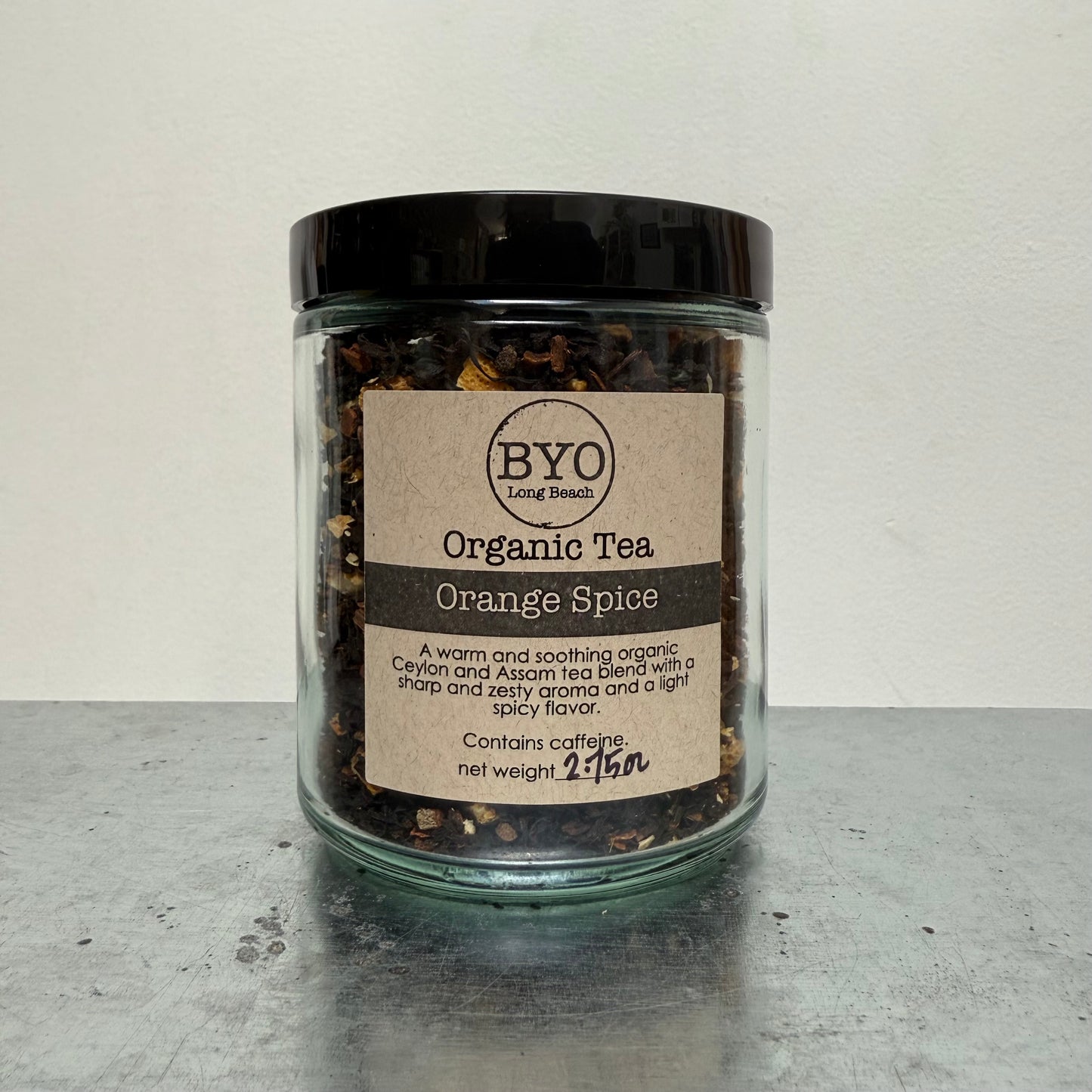 Jar of organic tea labeled 'Orange Spice' by BYO on a gray surface.