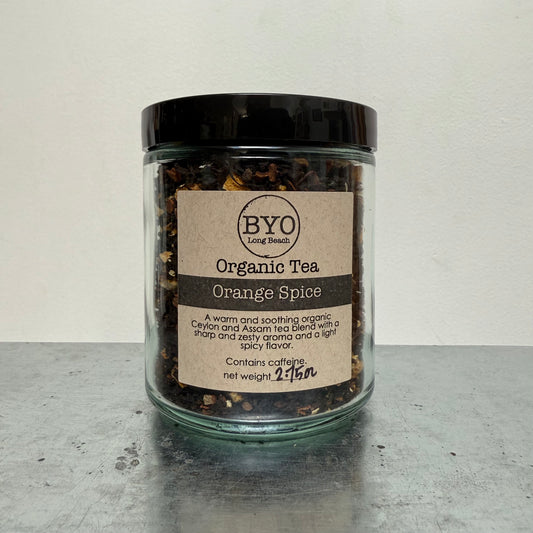 Jar of organic tea labeled 'Orange Spice' by BYO on a gray surface.