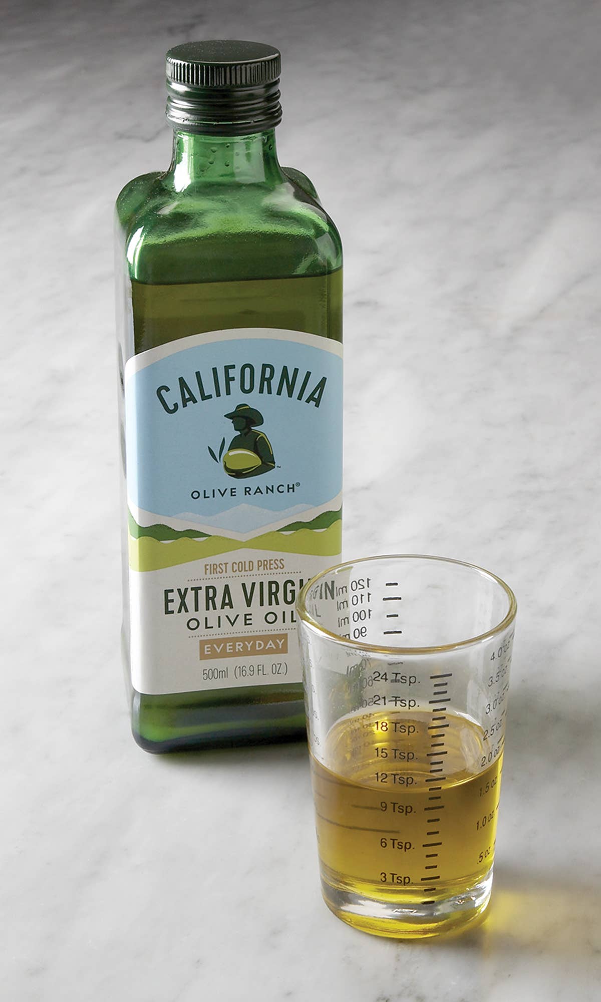 Bottle of California Olive Ranch olive oil with a glass of olive oil on a marble surface