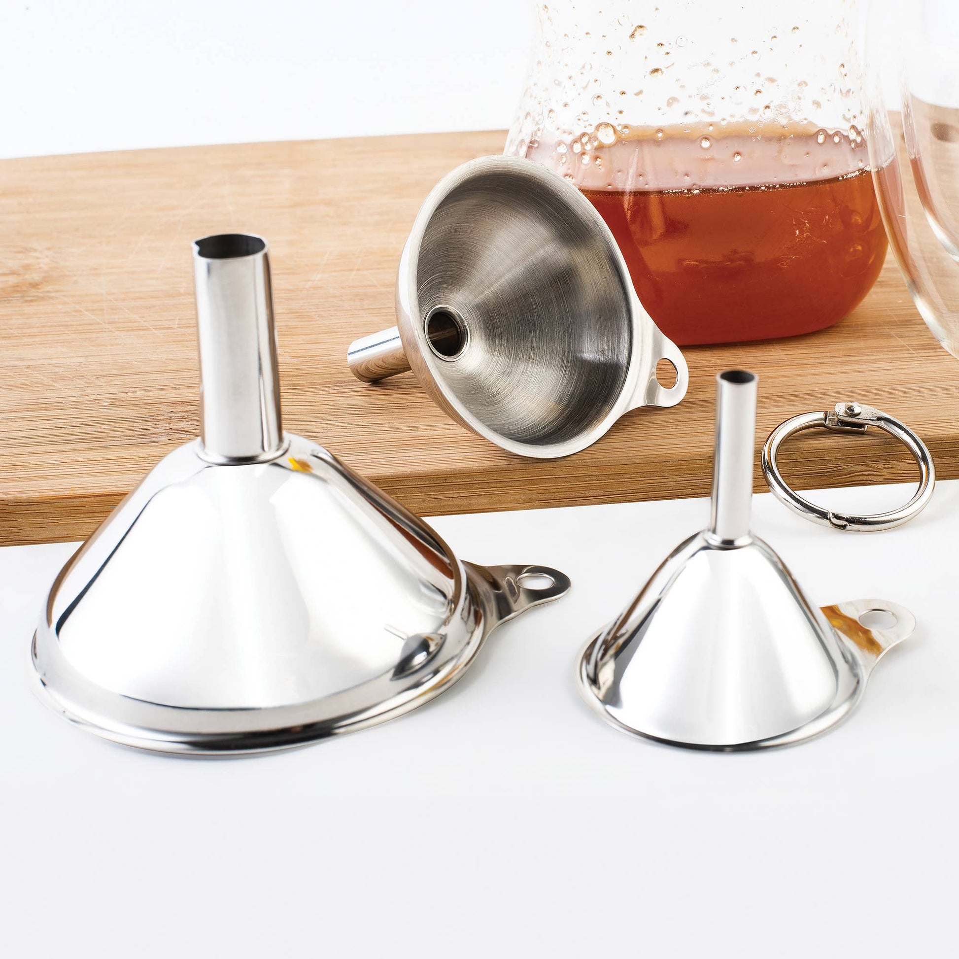 Set of metal funnels on a white surface with a wooden board in the background.