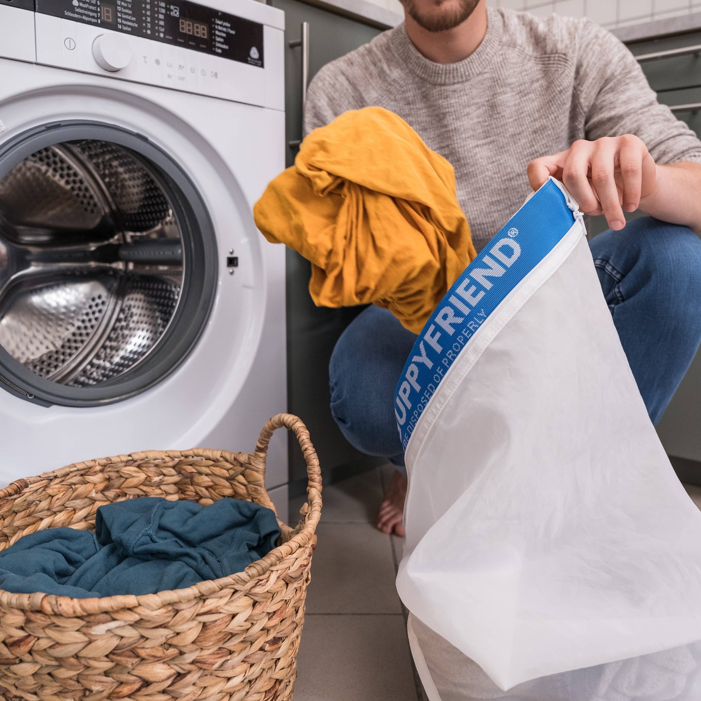 Person holding a laundry bag labeled 'Happyfriend' next to a washing machine and basket of clothes.