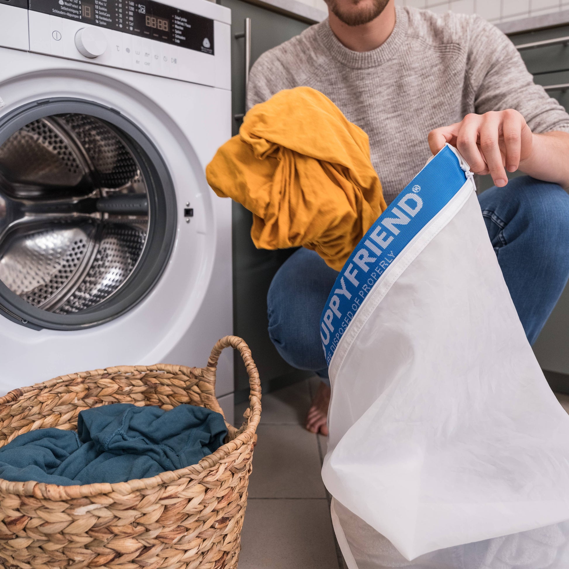 Person holding a laundry bag labeled 'Happyfriend' next to a washing machine and basket of clothes.