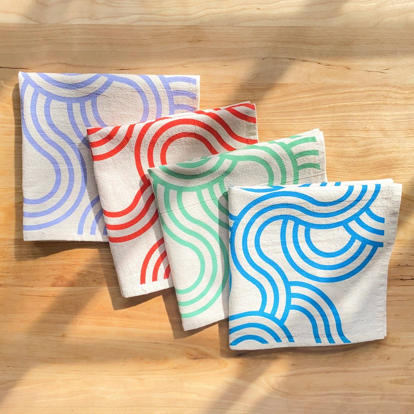 Four fabric napkins with colorful wave patterns on a wooden surface