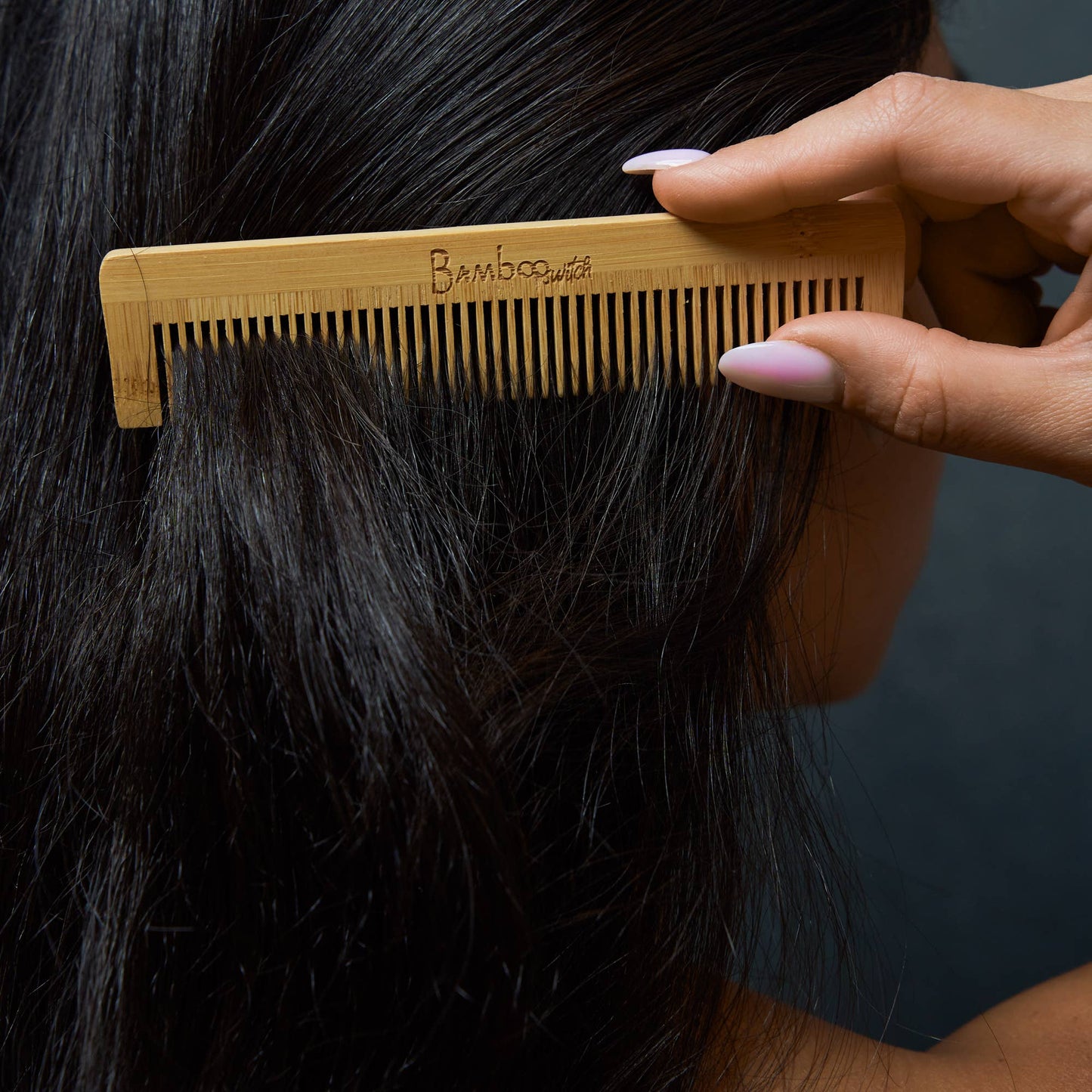 Person using a bamboo comb on their hair against a dark background