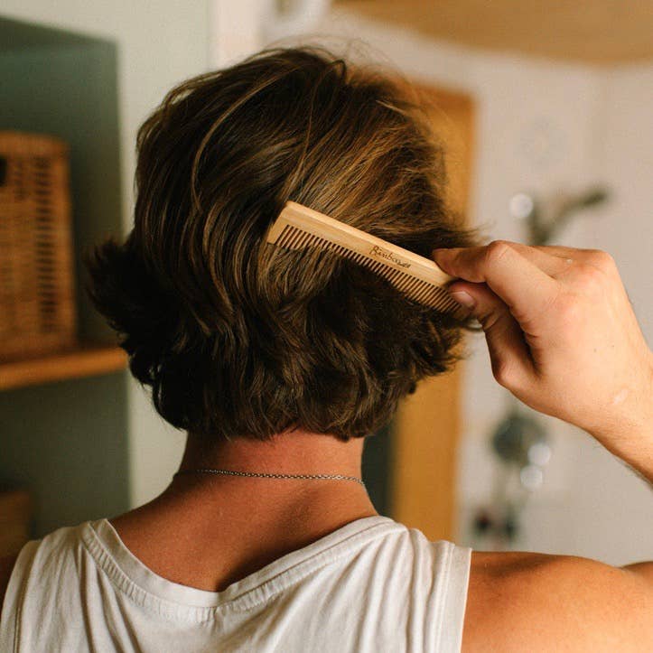 Person combing their short hair with a wooden comb in a bathroom setting