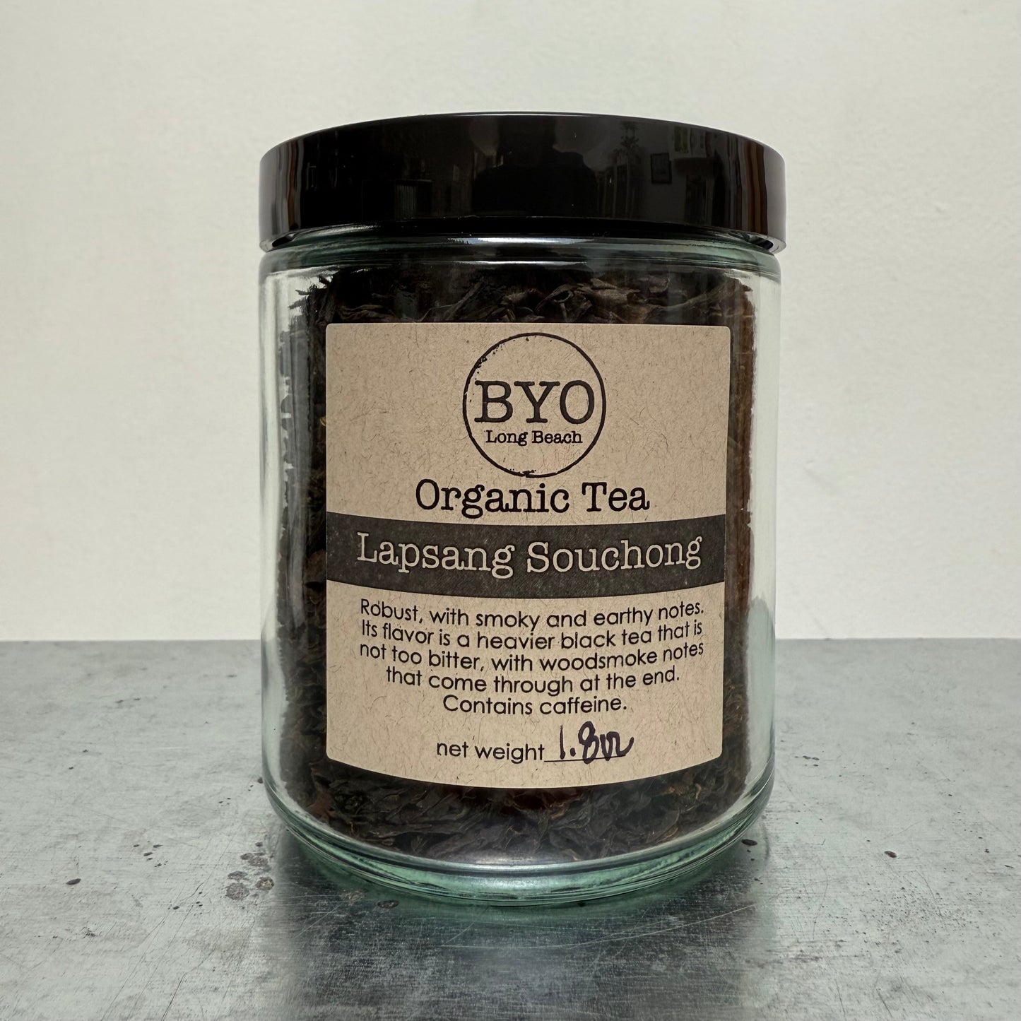 Glass jar of organic Lapsang Souchong tea with a label on a gray surface.