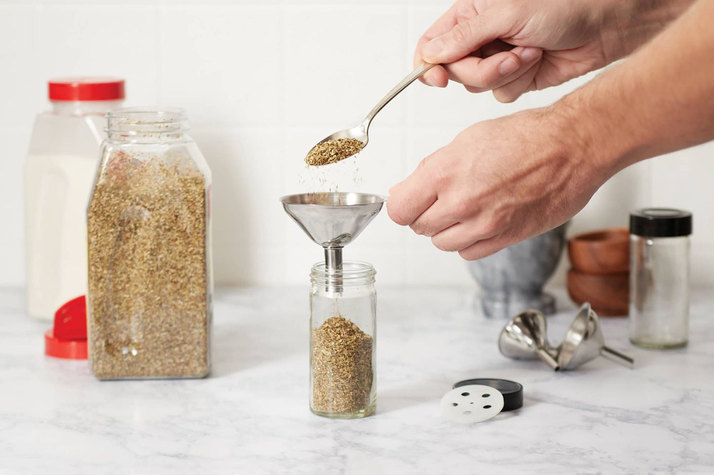 Person measuring and transferring spices using a funnel and spoon on a marble surface.