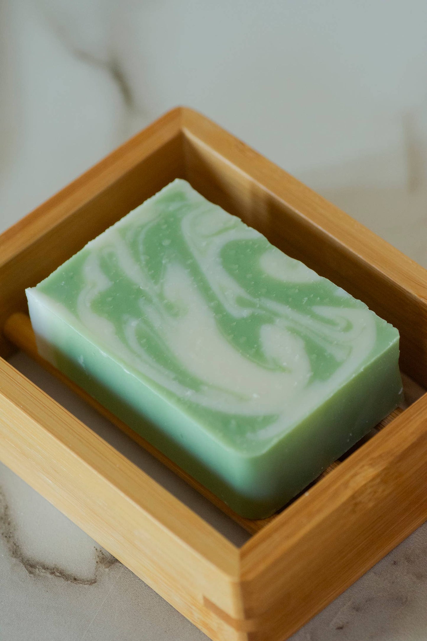 Green and white swirled soap bar in a wooden dish on a marble surface