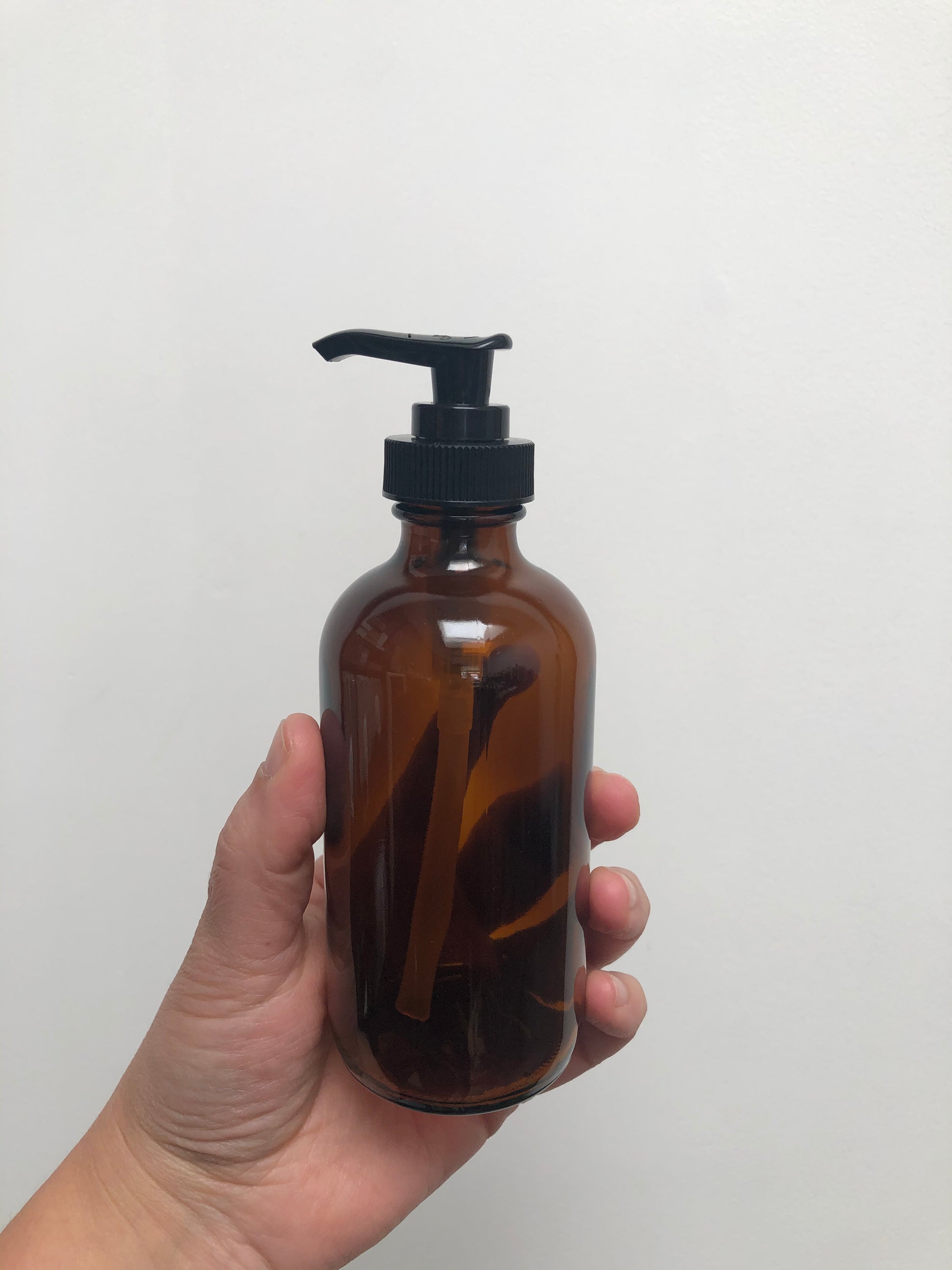 A hand holding a brown glass bottle with black plastic pump top